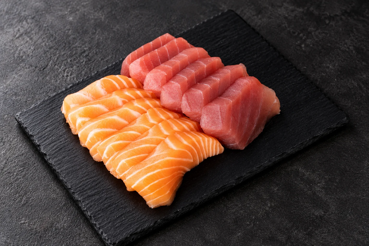 Sashimi saumon et thon sur une ardoise noire, fond sombre.