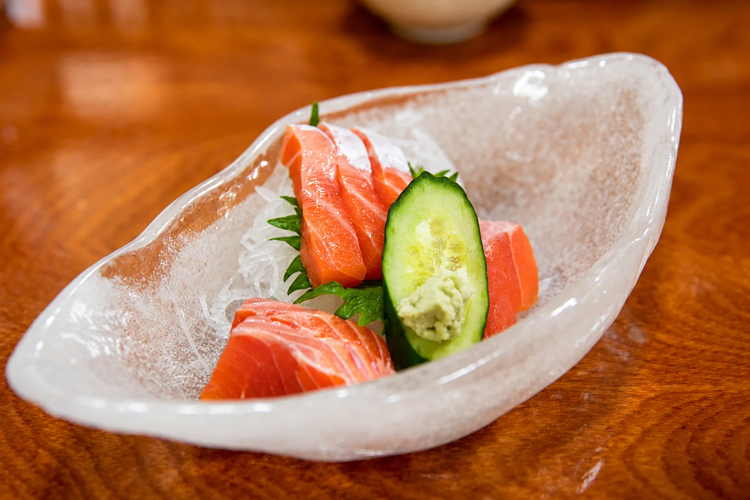 Tranches de saumon et concombre dans une coupe en verre, sur une table en bois.